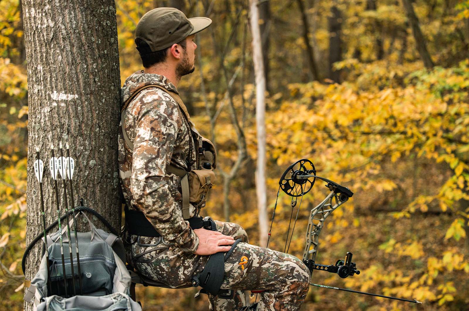 An bowhunter in a tree stand with yellow leaves in the background.