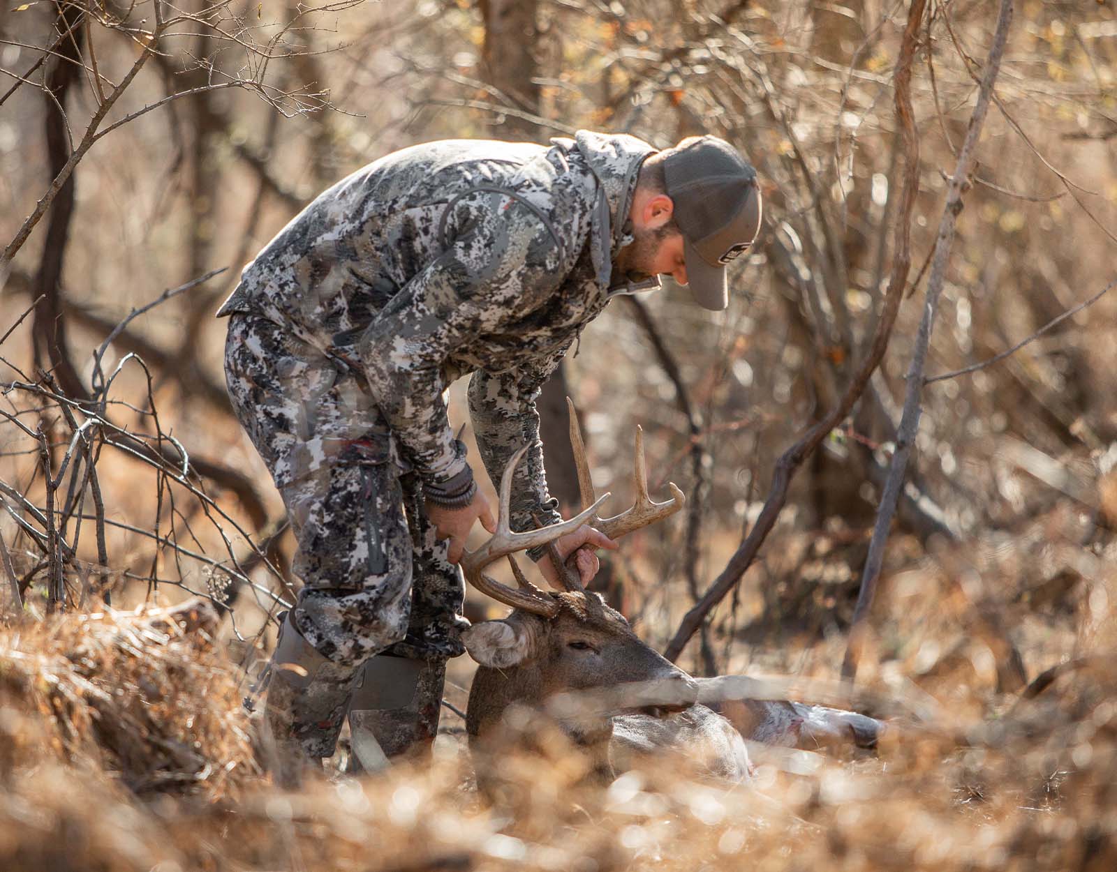 A deer hunter holds the antlers of a fallen deer.