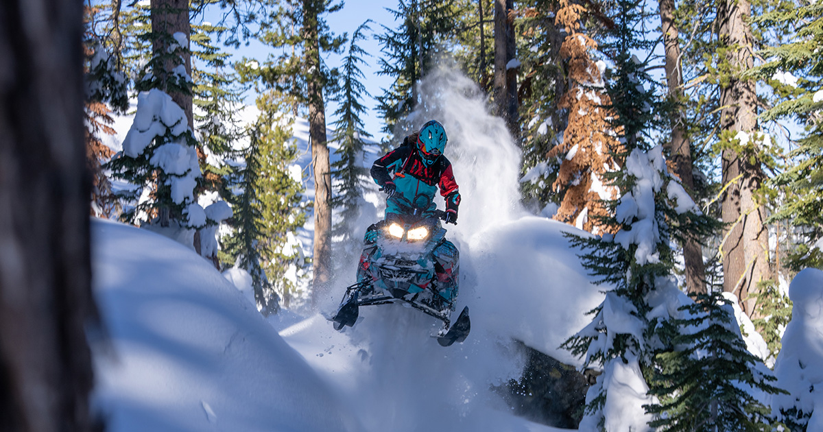 a person snowmobiling on a trail through trees